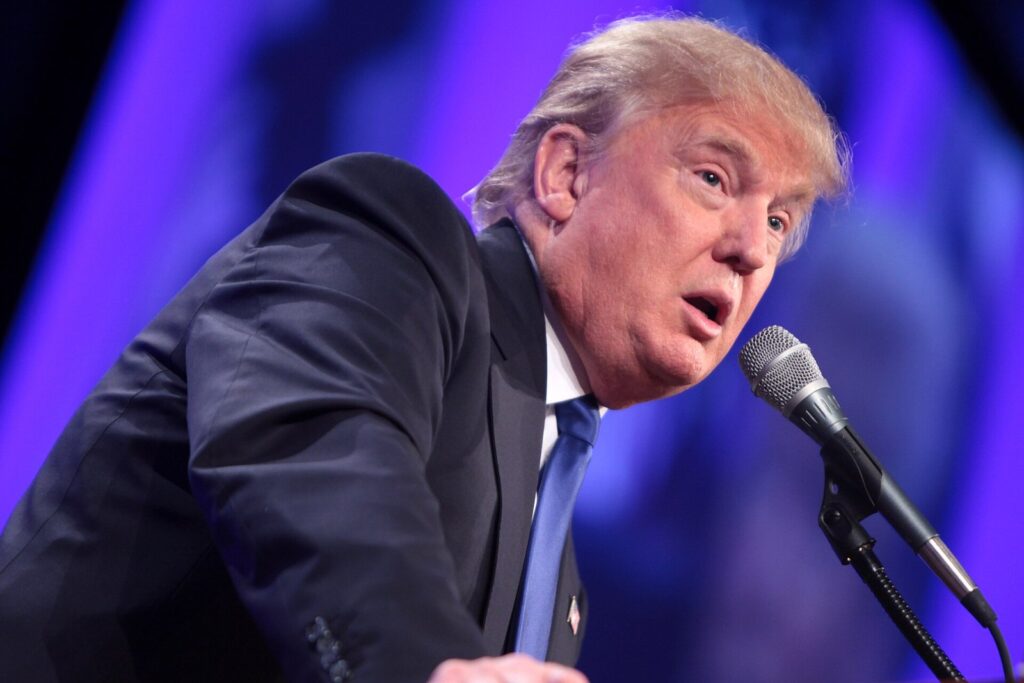Donald Trump beugt sich mit verzogenem Mund über ein Rednerpult-Mikrofon